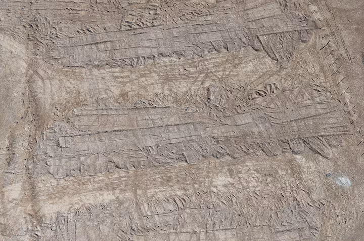 Pemandangan dari drone memperlihatkan jejak roda buldoser di atas tanah yang menutupi sebuah parit pemakaman di kuburan massal di padang pasir timur Suriah, dekat kota Dhumair, 27 Februari 2025.Investigasi Reuters menemukan bahwa pemerintah Assad secara diam-diam mengangkut ribuan jenazah ke lokasi ini dari kuburan massal terbuka di pinggiran Damaskus, Qutayfah, pada periode 2019–2021. REUTERS/Khalil Ashawi