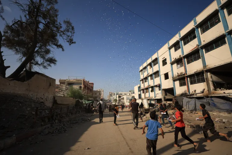 Warga Palestina berlari mengumpulkan selebaran [Dawoud Abu Alkas / Reuters]